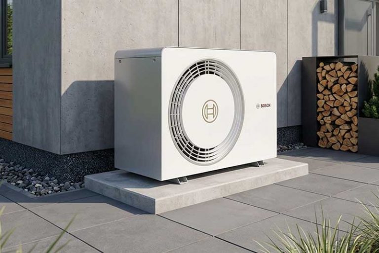 Eine moderne, weiße Luft-Wasser-Wärmepumpe von Bosch, die als Außeneinheit fachgerecht auf einem Betonsockel auf einer grauen Fliesenterrasse vor einer modernen Hausfassade installiert ist.