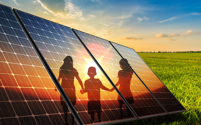 Solarmodul auf einer Wiese, auf dem sich drei Kinder und ein Sonnenuntergang spiegeln