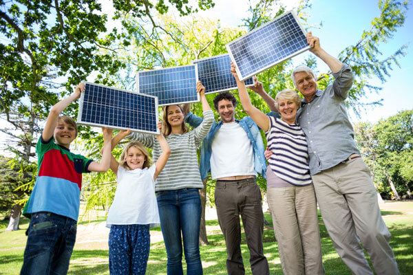 Großvater, Großmutter, Vater, Mutter und zwei Kinder stehen im Garten und halten Solarmodule in die Höhe